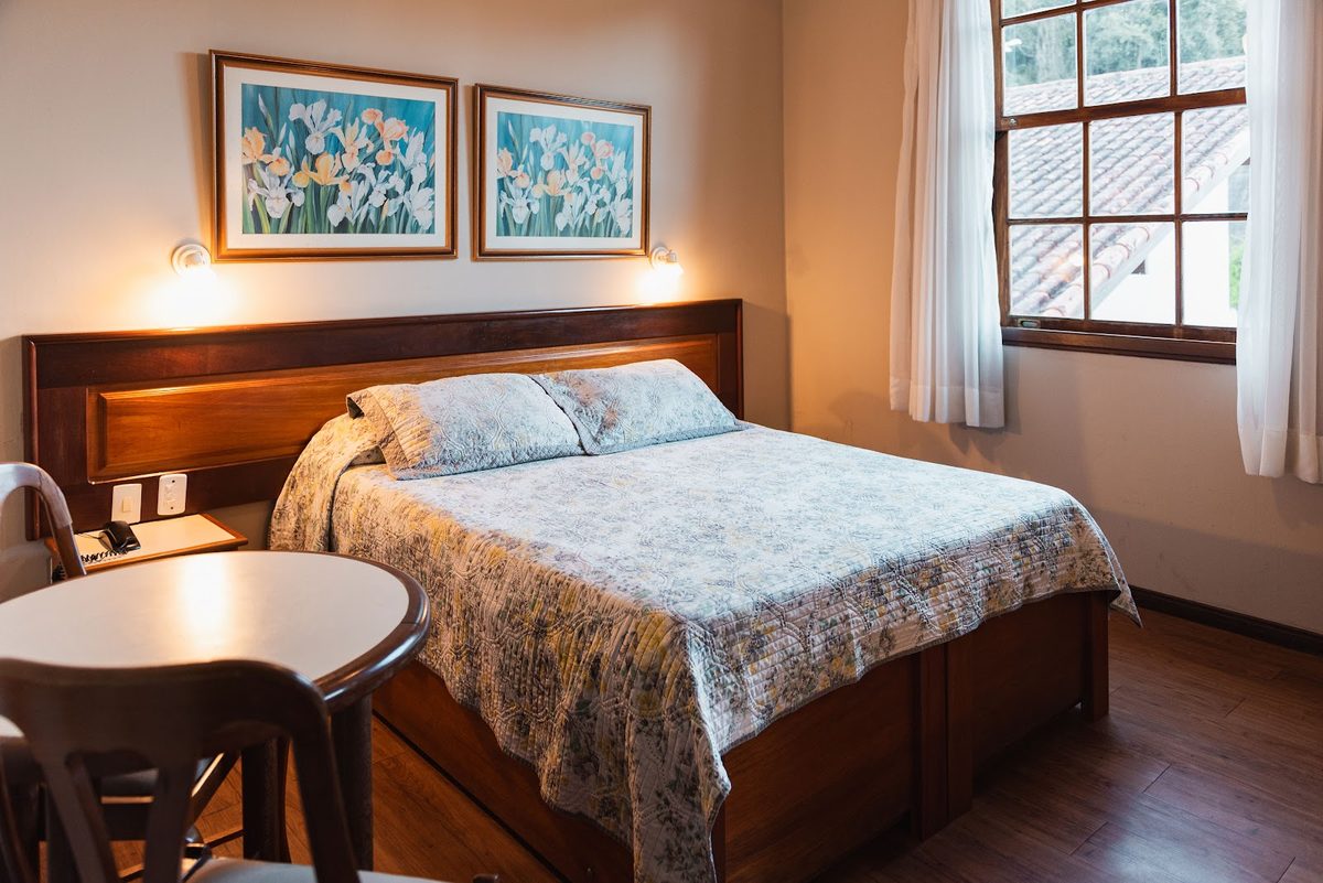 Quarto Colonial com cama de casal, quadros e piso de madeira